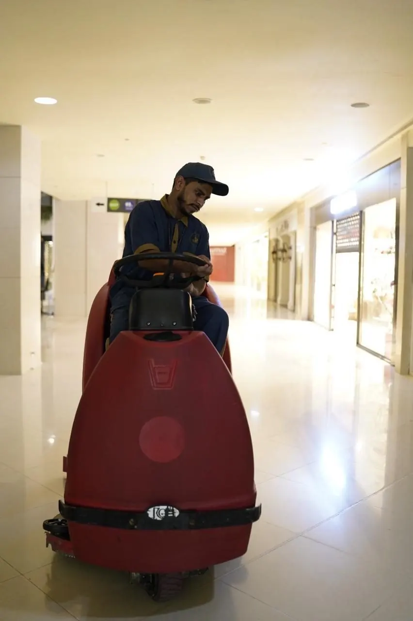Operator on a red ride-on scrubber cleaning a mall floor